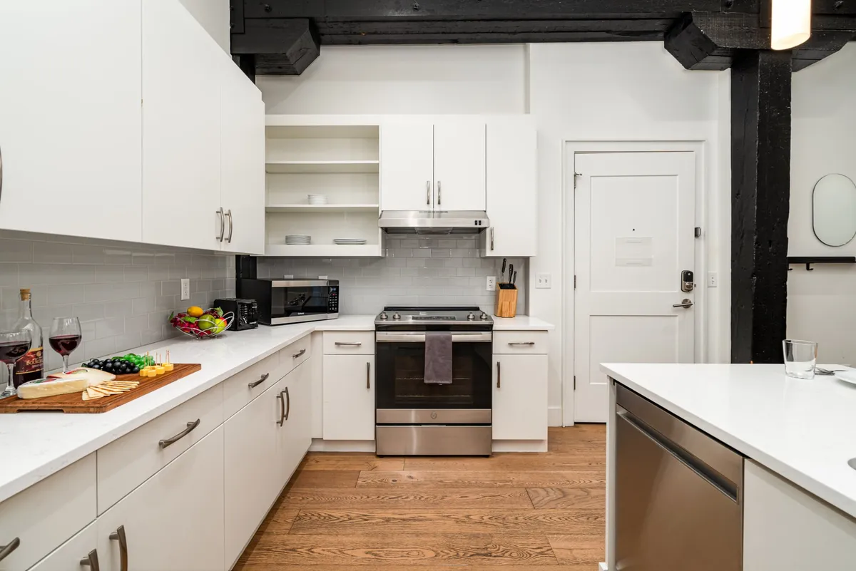 A stylish kitchen scene with an island, stainless steel appliances, a wooden cutting board with cheese and fruit, and wine glasses. The setup hints at entertaining, prepping charcuterie, and enjoying drinks—directly linking to the text’s mention of social snacking and cocktail mixing.