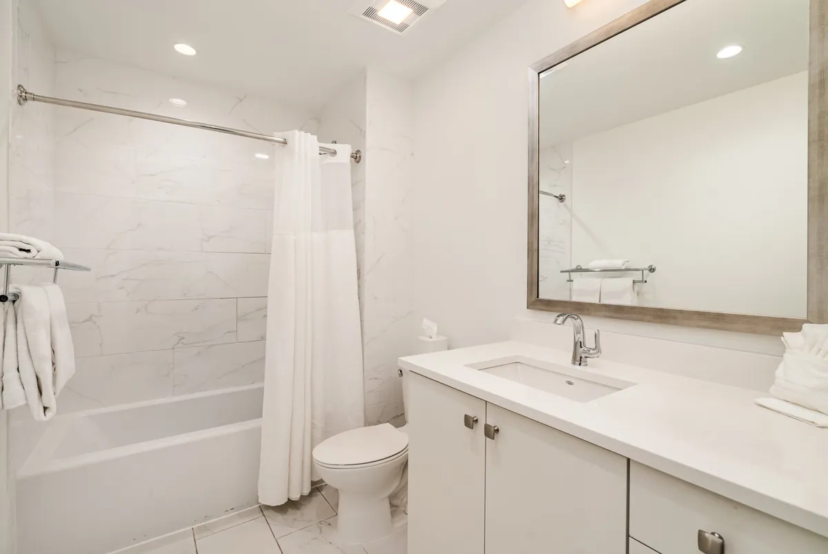 A tranquil, modern bathroom featuring a bathtub, single vanity, mirror, and toilet. The space is bright and streamlined, evoking a spa-like atmosphere ideal for relaxation and daily routines.