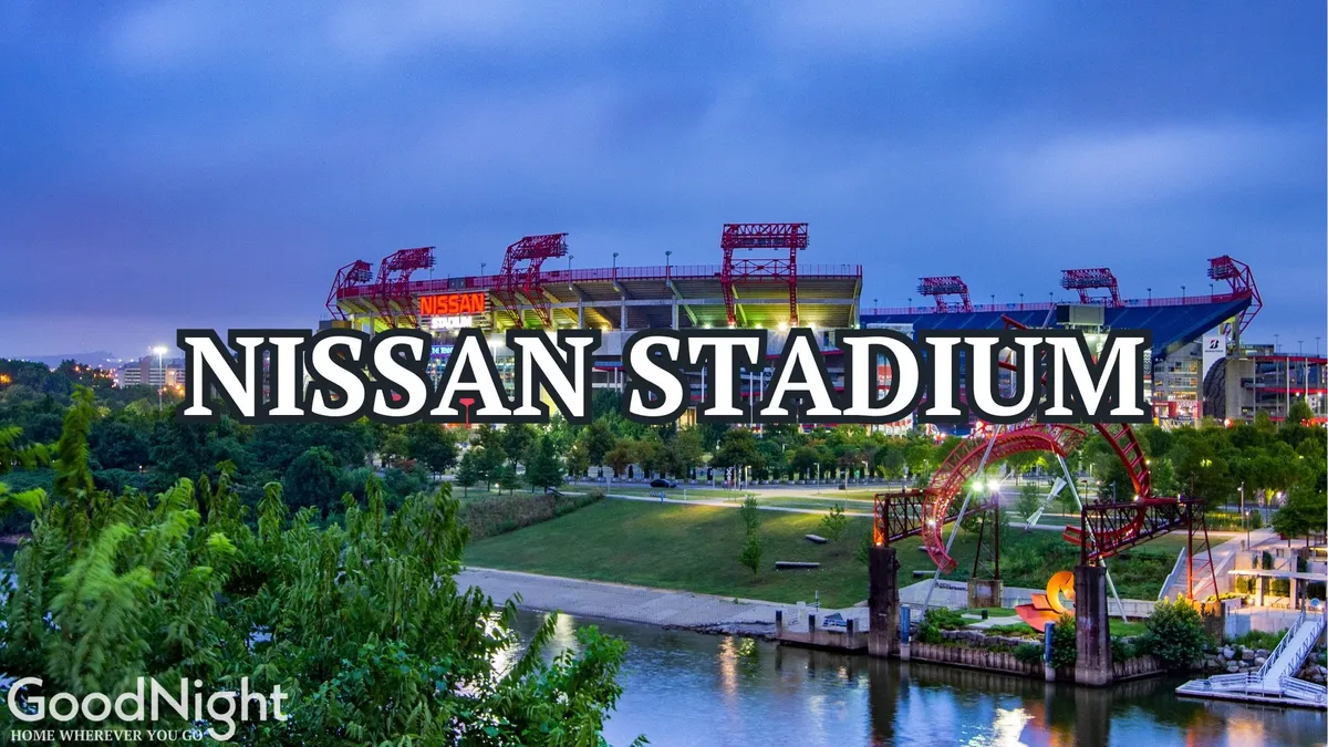 This exterior shot features Nissan Stadium, a major sports venue in Nashville, prominently situated along the riverfront park with lush greenery framing the scene. The stadium is bathed in sunset light, conveying the energy and excitement of live sports and entertainment events that often draw large crowds to the area.